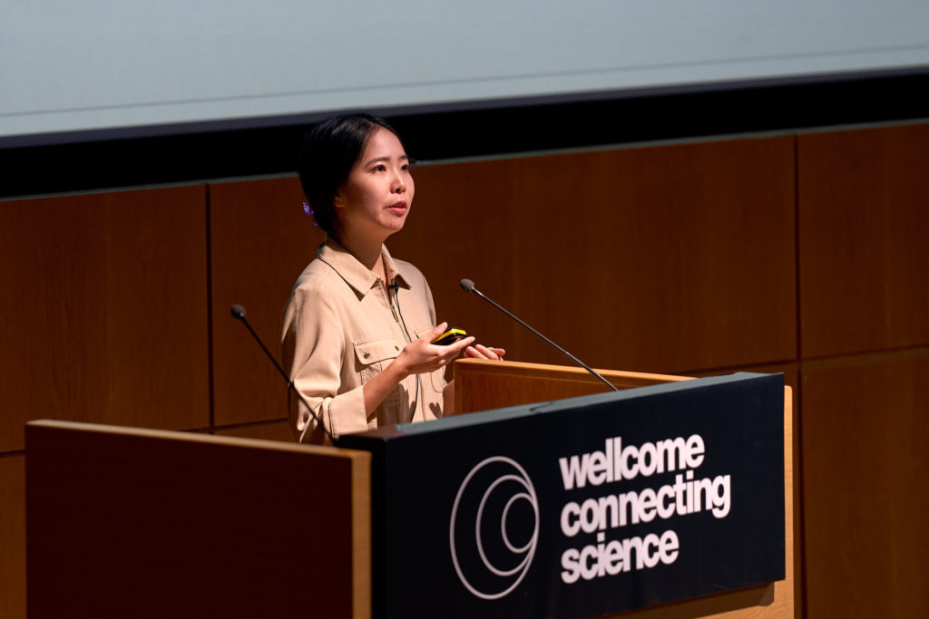 Colour photo of a female speaker delivering a talk during a CRISPR conference session. Speaker podium displays the Wellcome Connecting Science logo