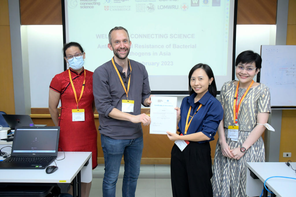 Colour photo of Polly Yap receiving her Certificate of Completion for the 2023 Antimicrobial Resistance course from instructor Dr Ewan Harrison. Also present in the photo: (Left) Dr Cassandra Soo - course instructor, (Right) Dr Claire Chewapreecha - course instructor. Photo credit: Mahidol University. 
