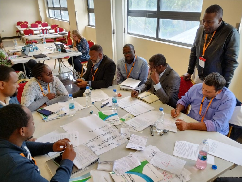 A colour photo of eight participants on our 2023 Establishing Capacity for Pathogen Genomics course, hosted by our regional training partners at the Ethiopian Public Health Institute, Addis Ababa, Ethiopia. The groups of scientists are working on a group activity around a large table. Photo credit: Liã Barbara Arruda, Education Developer, Wellcome Connecting Science.