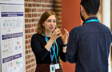 Two conference delegates attending a poster session. One delegates is explaining the poster content to the second person.
