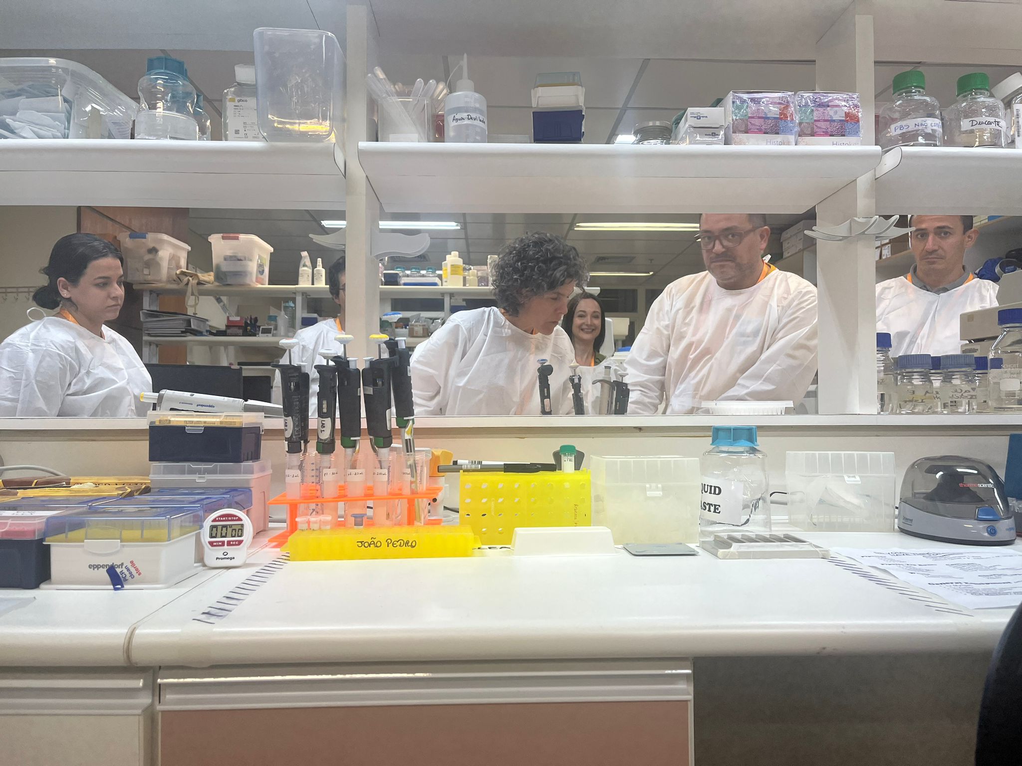 Six course participants engaged in practical laboratory training, at the INCA lab facility. They are all wearing traditional white lab coats. 