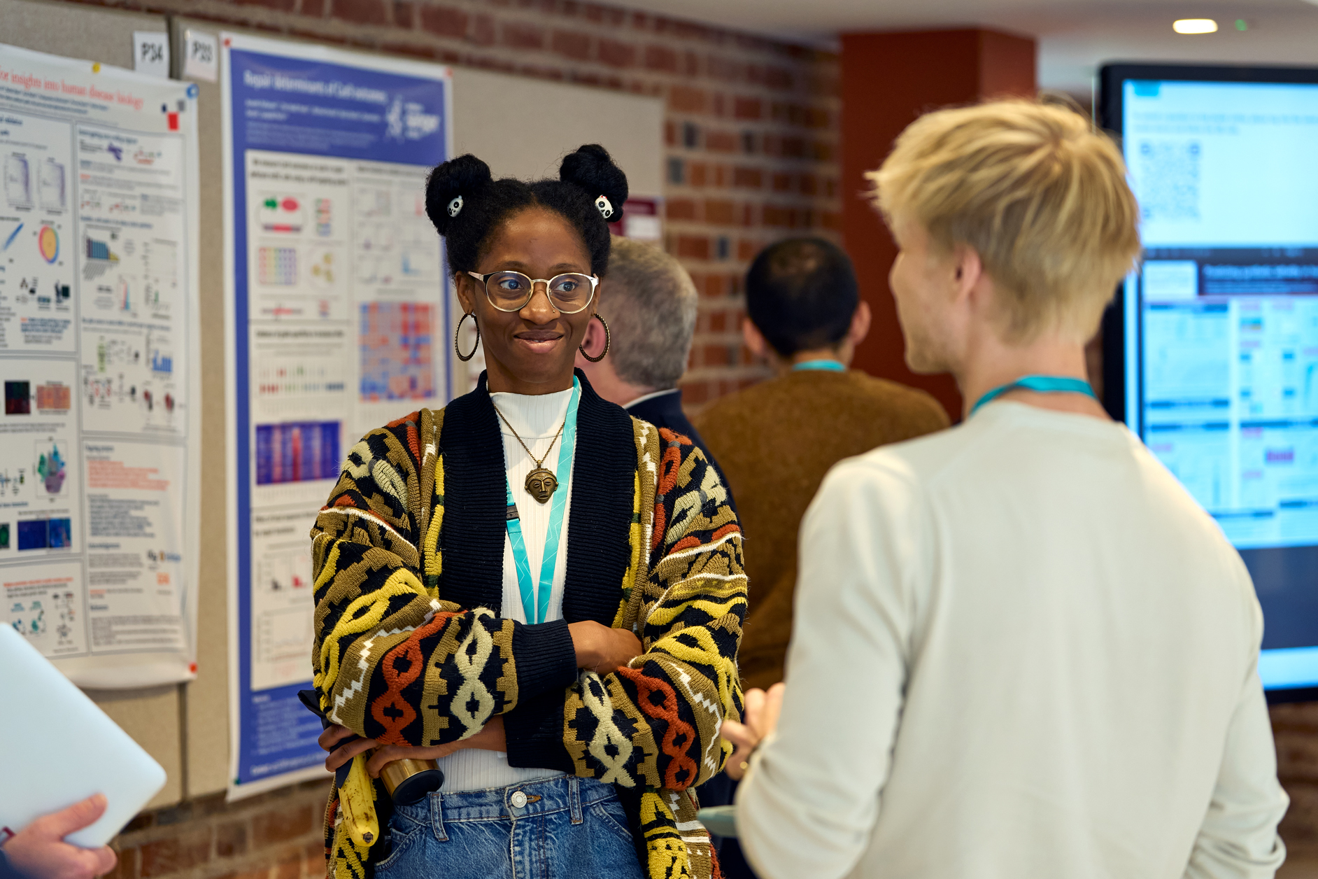 Two conference delegates engaged in conversion during a networking break. They are standing near a series of scientific posters pinned to boards. A digital poster board is also in view. Image credit: Ben McDade Photography for Connecting Science. 