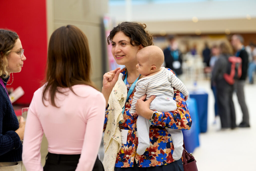 A group of conference delegates standing during a networking session. One is holding a baby.