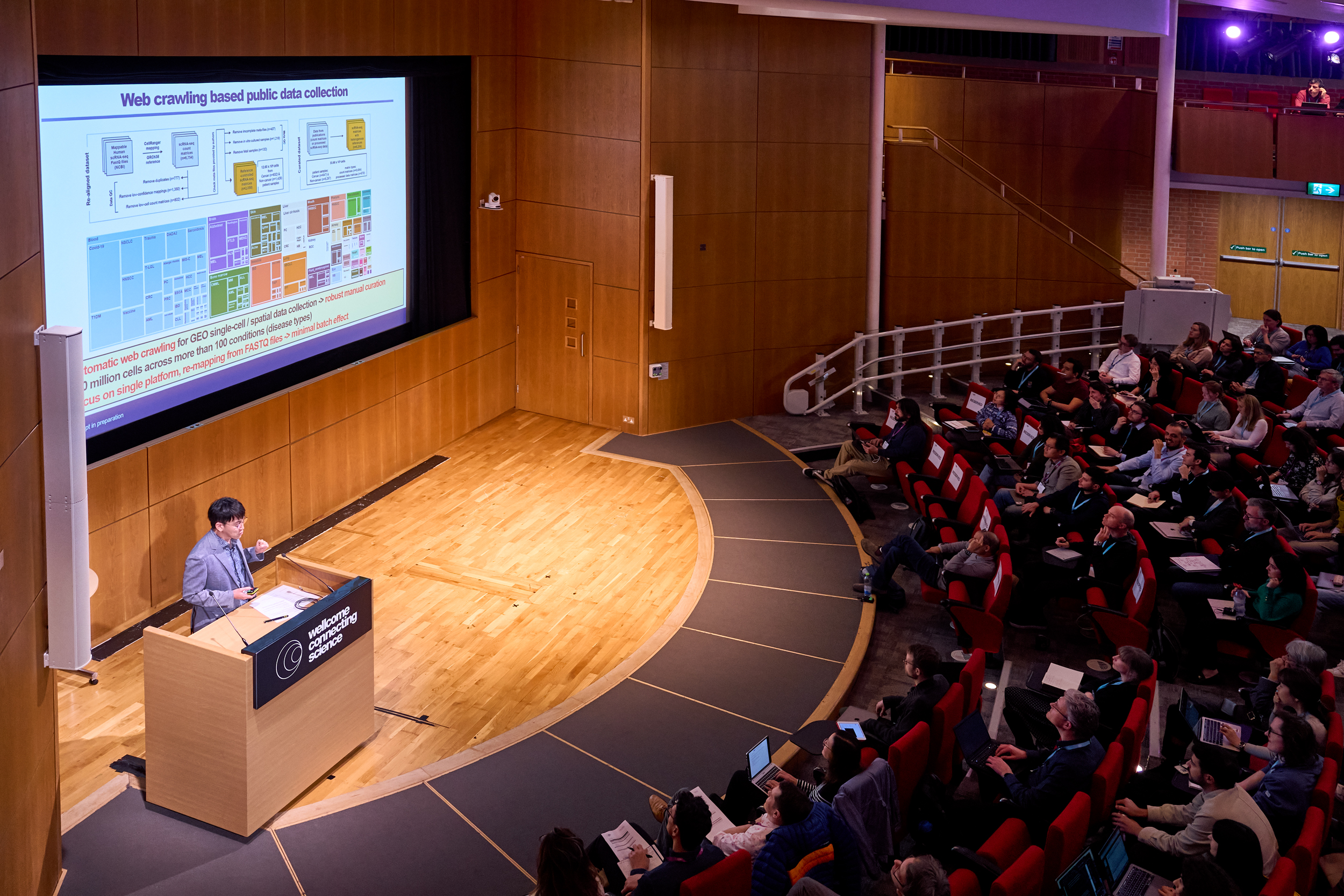 A conference speaker presenting their slides on a stage. They are standing behind a podium.