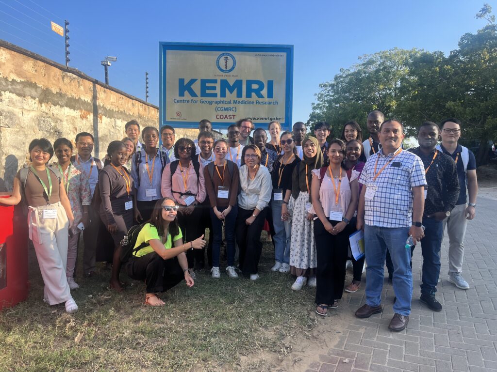 Course participants posing for a photo on a grass verge outside the KEMRI Centre for Geographical Medicine Research