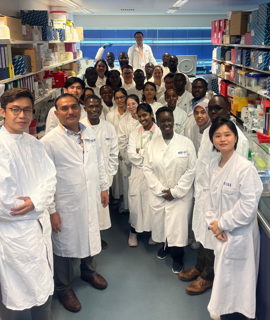 Course participants posing for a group photo in a training laboratory. they are wearing white coats. 