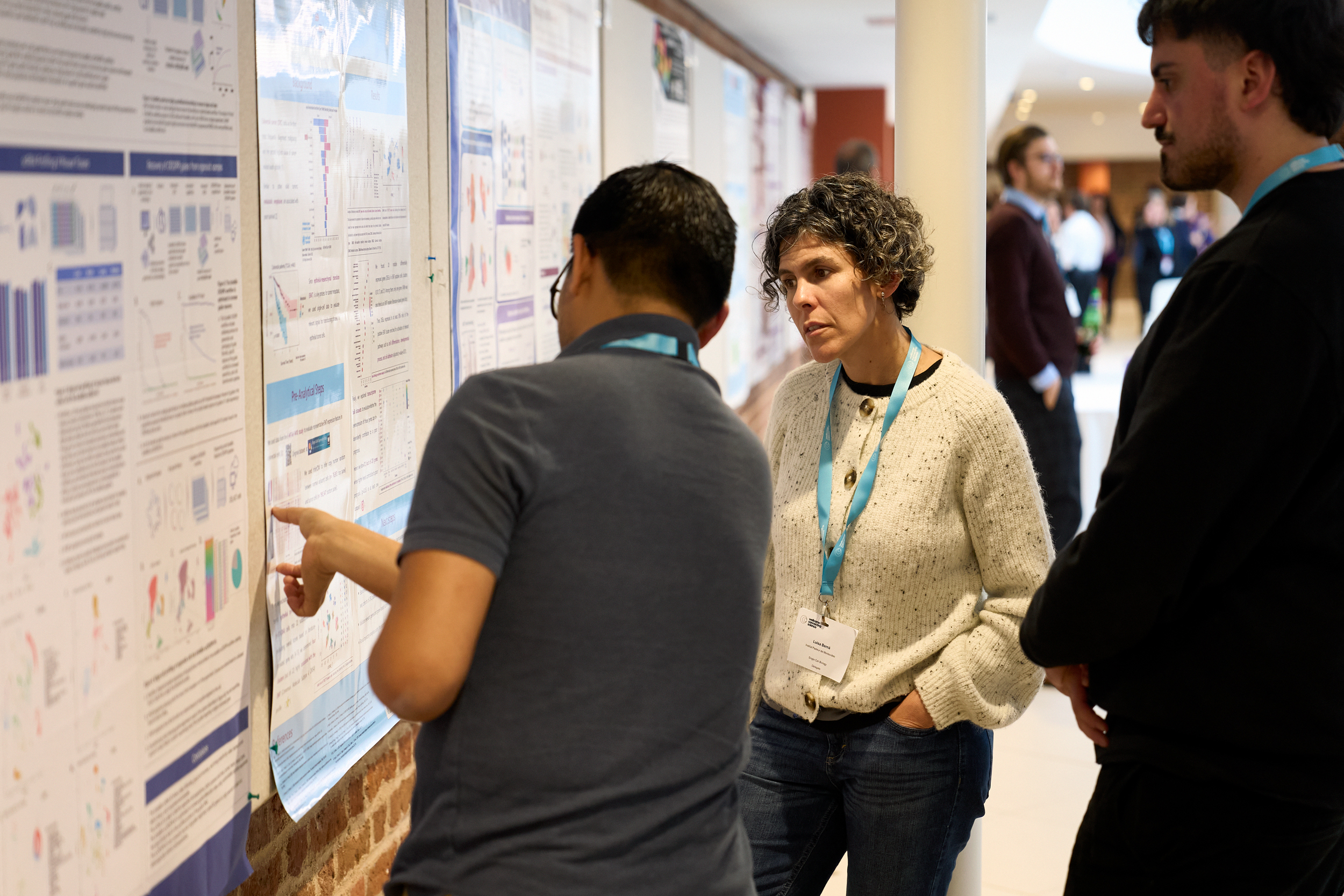 Three conference delegates observing a scientific poster. One delegates is explaining the content to the others.