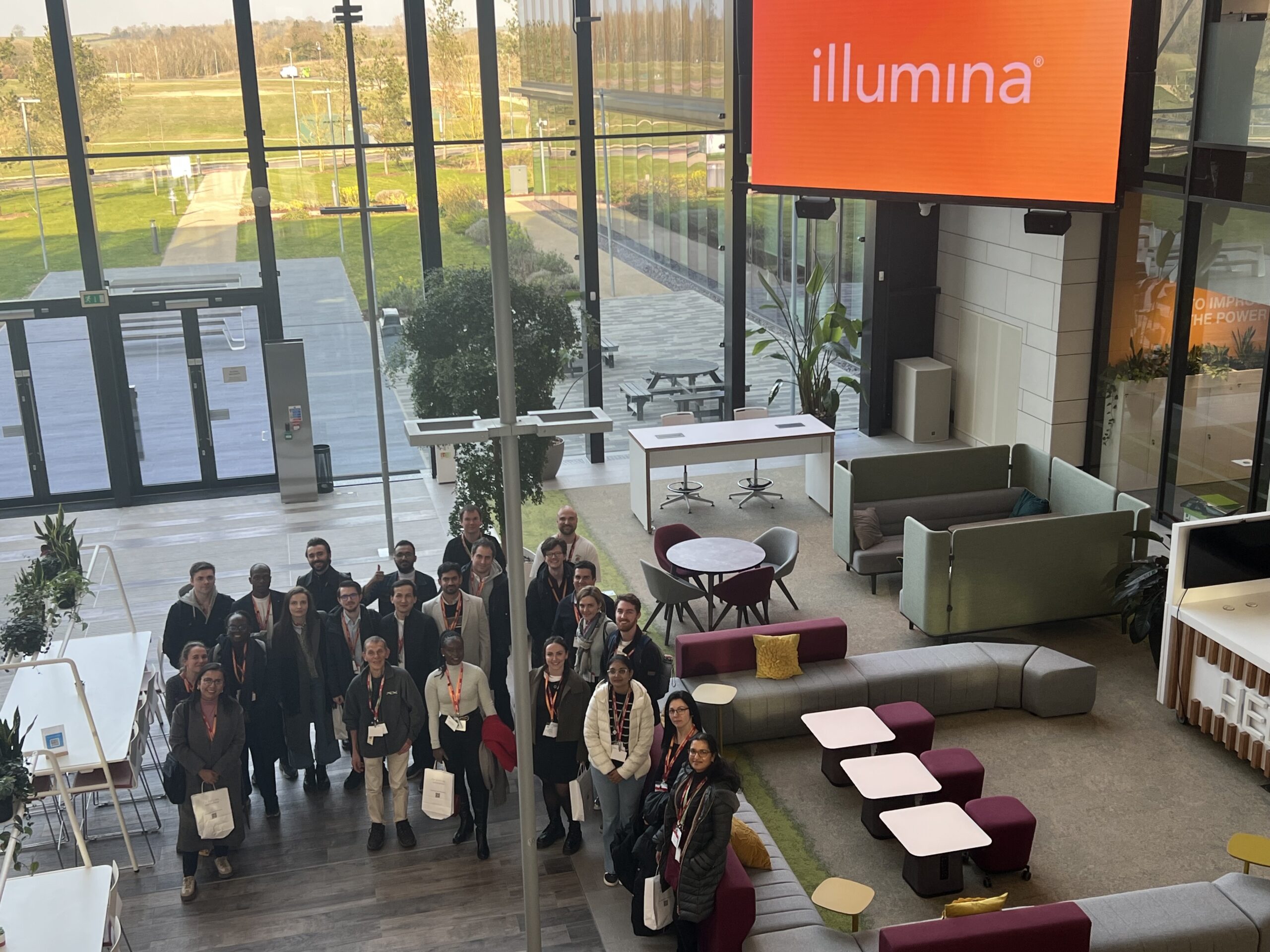 Course participants and instructors standing in the welcome lounge at the Illumina Centre, Cambridge, UK.