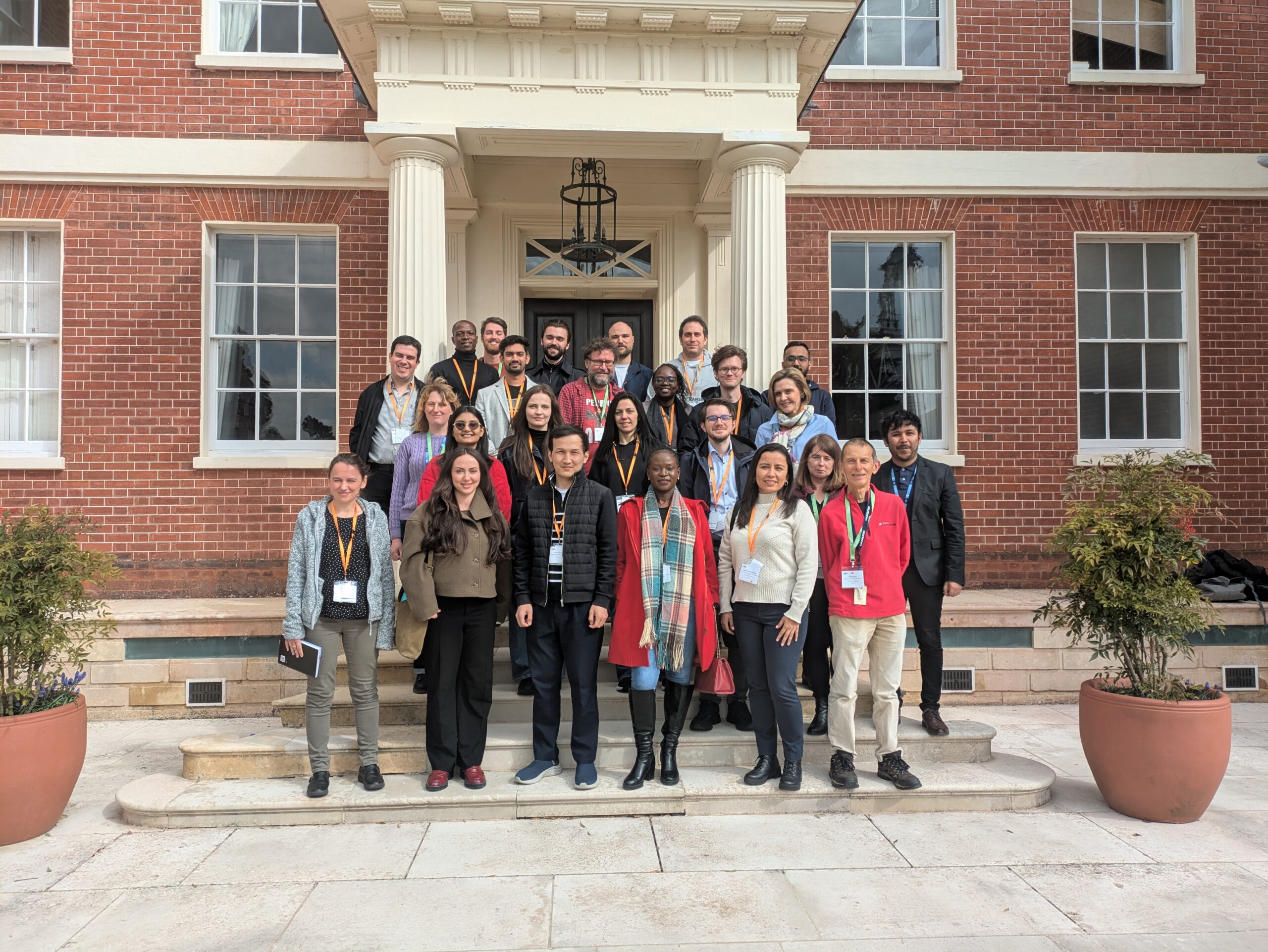 Course participants and instructors standing on the stone steps leading up to the front entrance to Hinxton Hall. They are posing for the 2024 course group photo.