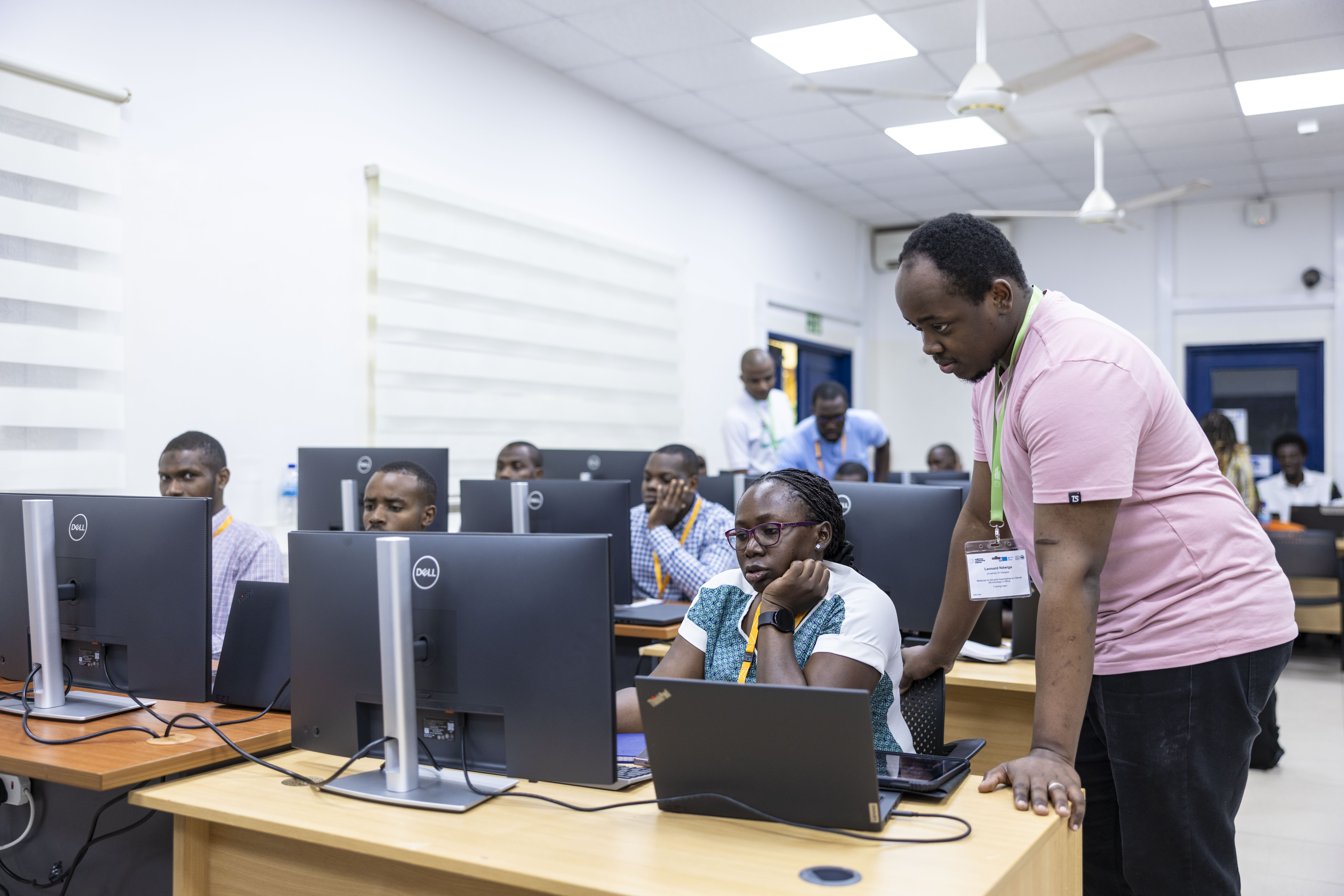 Instructor assists a participant in a computer classroom where several other course attendees work at desktop computers during a bioinformatics training session.